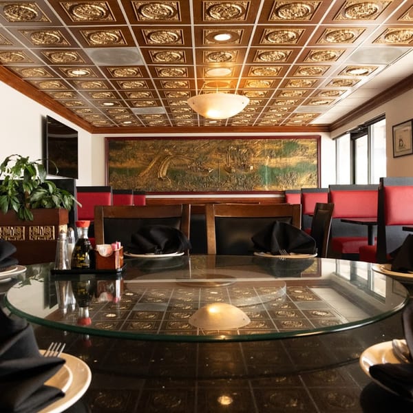 A dining room at Shanghai Garden with a glass-top table, red booths, and an ornate gold ceiling.