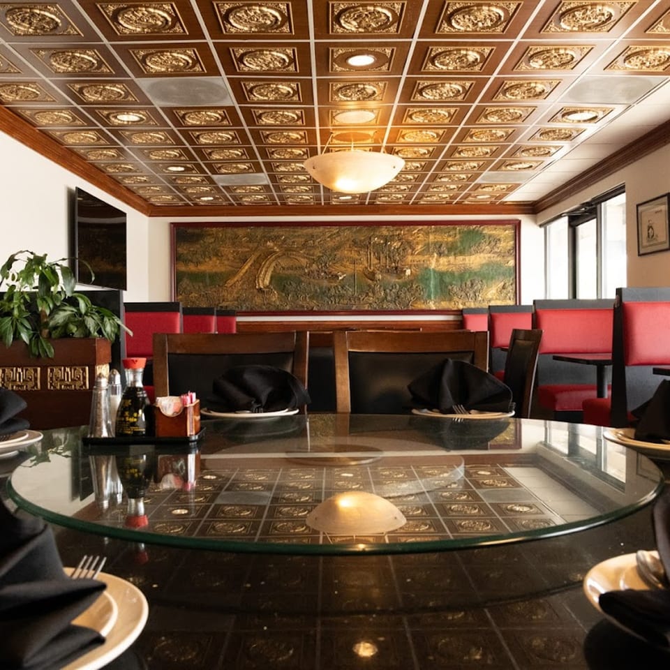 Interior of Shanghai Garden restaurant with a glass table, red booths, and ornate golden ceiling tiles.