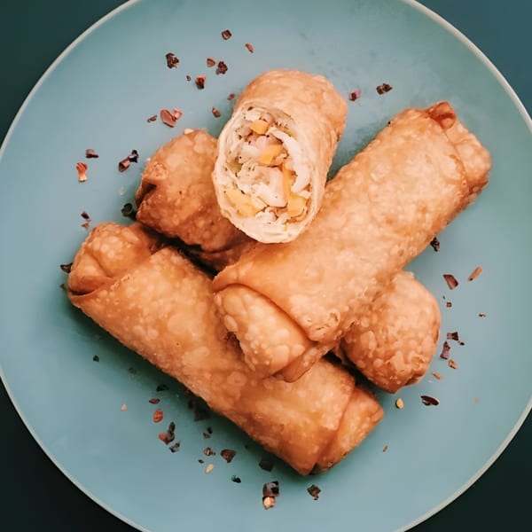 Golden-brown Shanghai Garden egg rolls, one cut open to show the vegetable filling, on a blue plate.