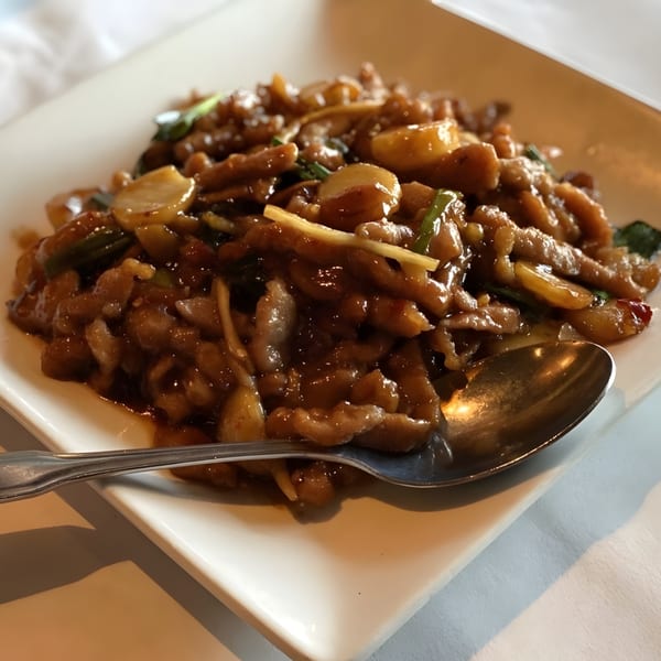 A close-up of a Chinese dish with sliced meat, mushrooms, and green onions in a rich brown sauce.