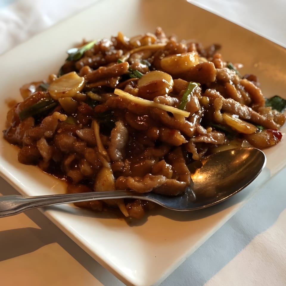 Close-up of a Chinese dish with sliced pork, mushrooms, and green onions in a rich brown sauce.