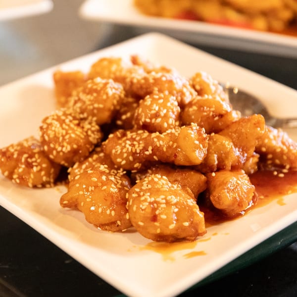 A white rectangular plate filled with golden-brown sesame chicken pieces in a sweet glaze.