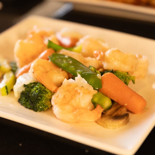 Shrimp and mixed vegetables, including broccoli, carrots, and snow peas, on a white rectangular plate.