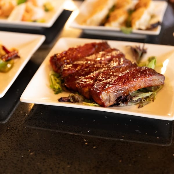 Shanghai Garden's glazed spare ribs on a bed of lettuce, with other dishes blurred in the background.
