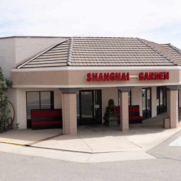 Exterior of Shanghai Garden restaurant with red signage, a tiled roof, and a stone lion statue.